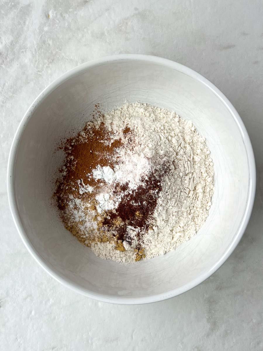 Flour, baking soda, baking powder, salt, and pumpkin pie spice in a white mixing bowl.